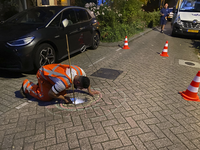 904892 Afbeelding van een medewerker van het waterleidingbedrijf Vitens tijdens de inspectie van een gat onder de ...